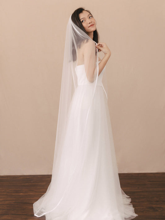 Woman wearing a white wedding dress with a veil against a beige background
