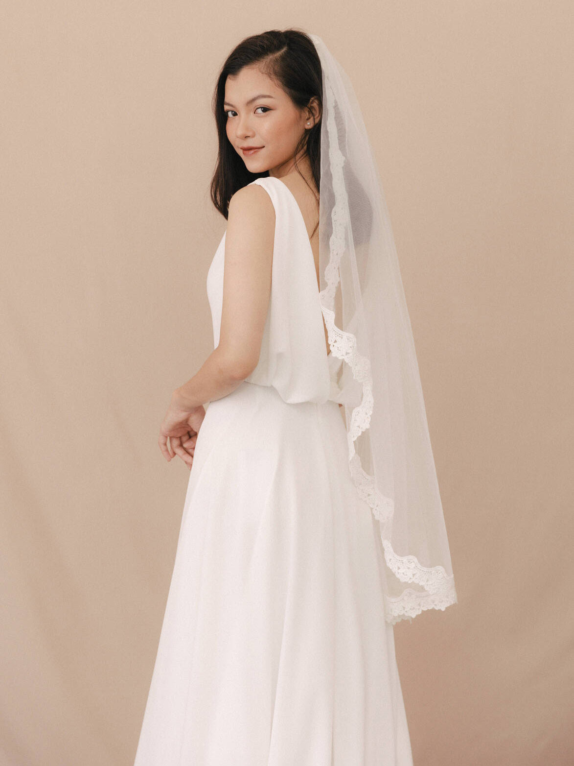 Woman wearing a white wedding dress with a veil against a beige background