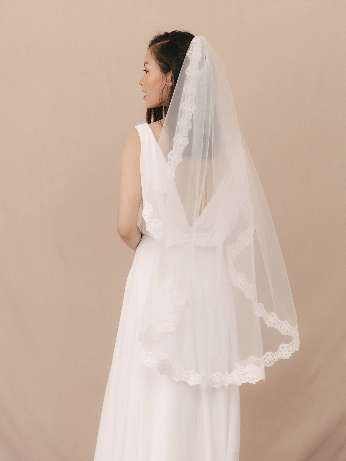 Woman wearing a white wedding dress with a veil against a beige background