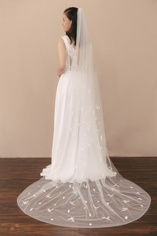 White wedding dress with a long train on a wooden floor against a beige wall.