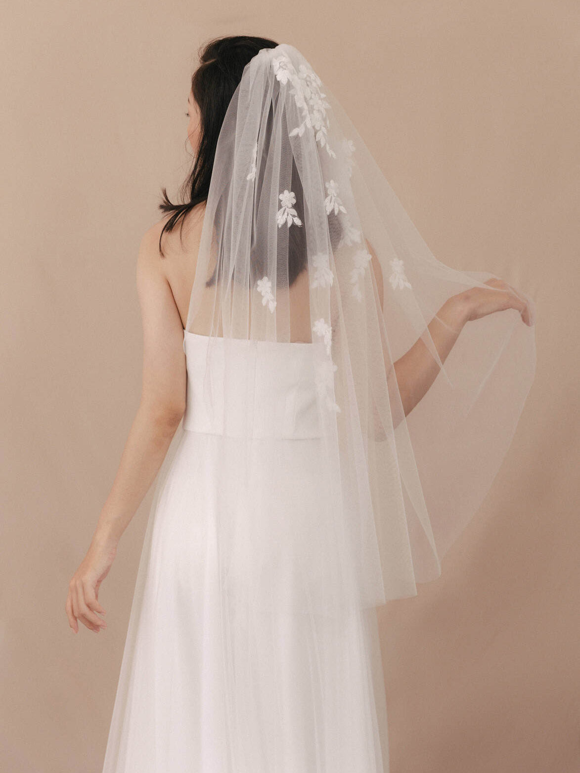 Bride wearing a white wedding dress and veil against a beige background