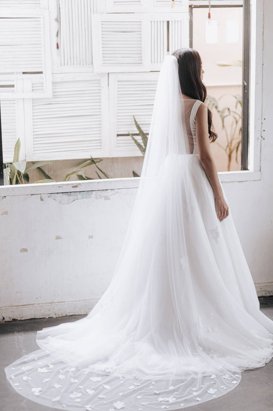 Woman in a white wedding dress with a long veil standing in a room with large windows.