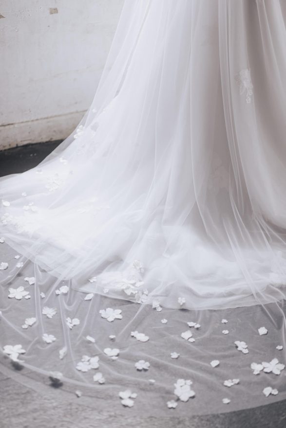 Close-up of a white wedding dress with floral details on a neutral background