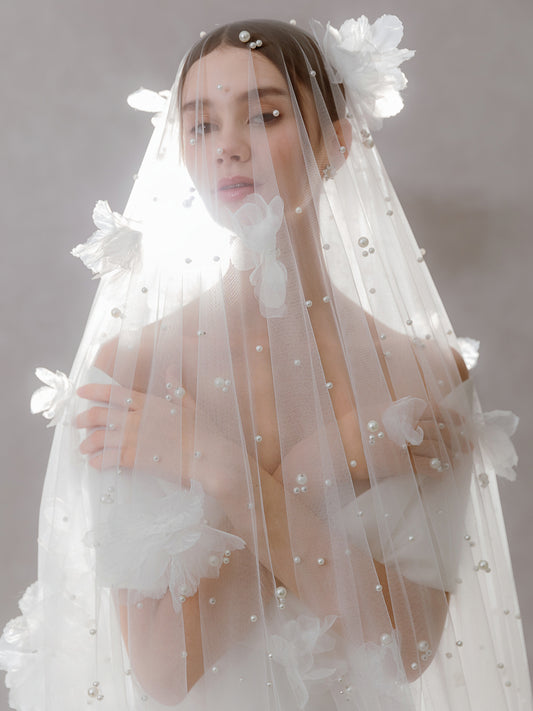 Woman wearing a delicate white veil with floral and pearl details on a neutral background