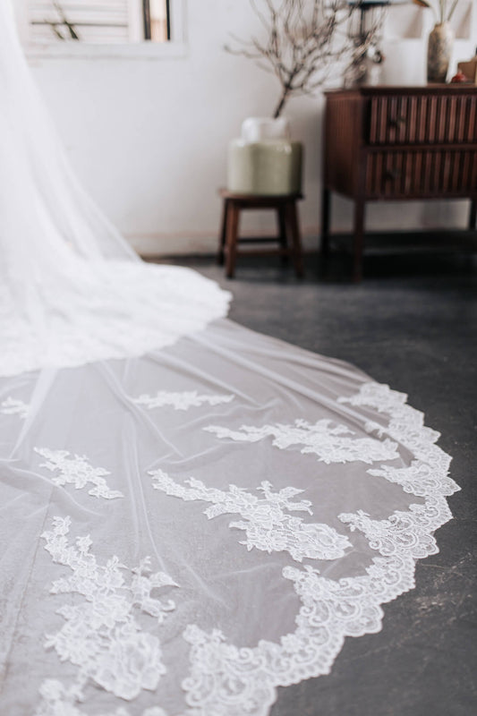 Close-up of a white lace wedding dress on a dark surface with a blurred indoor background.
