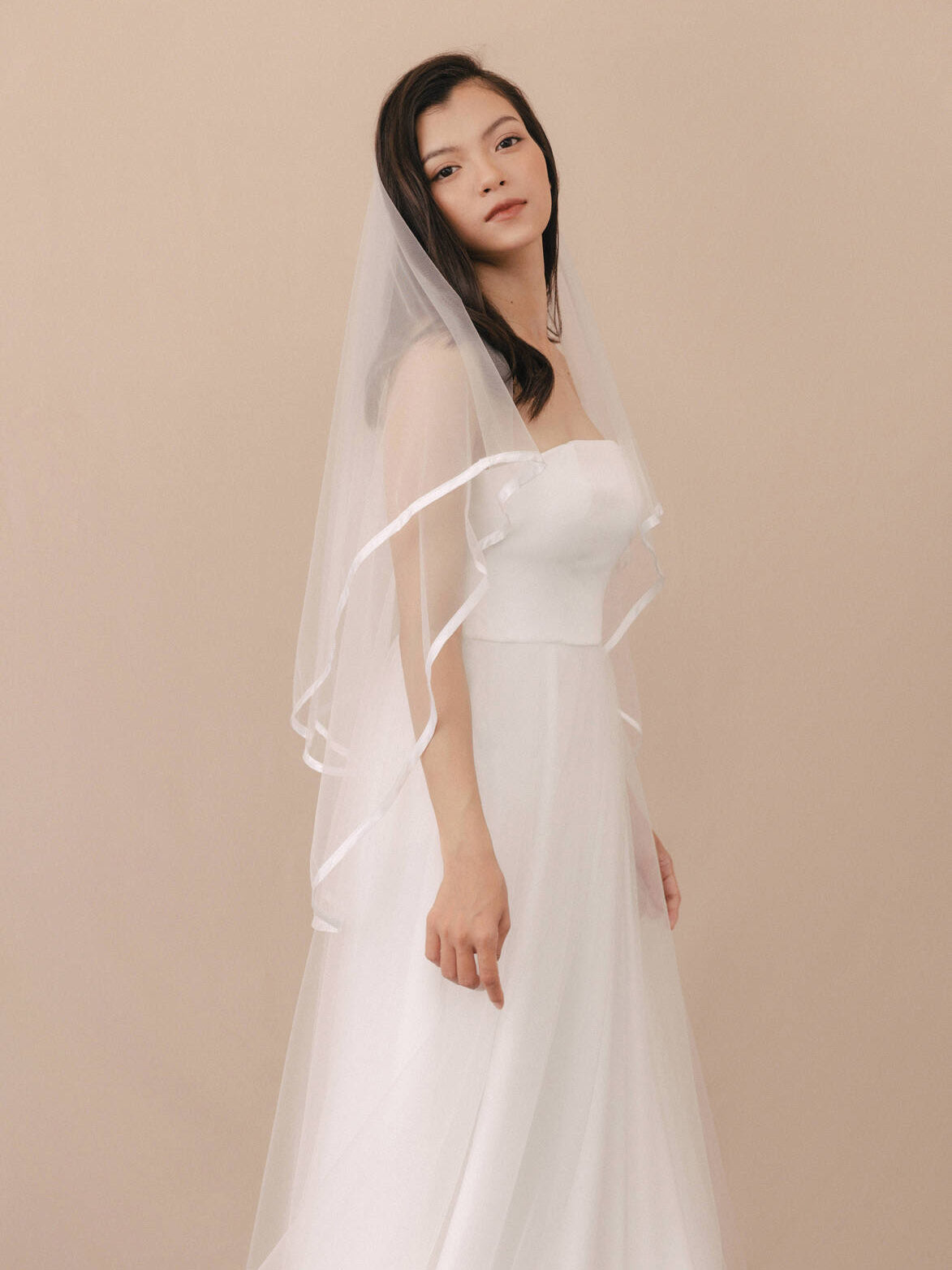 Woman wearing a white wedding dress with a veil against a beige background