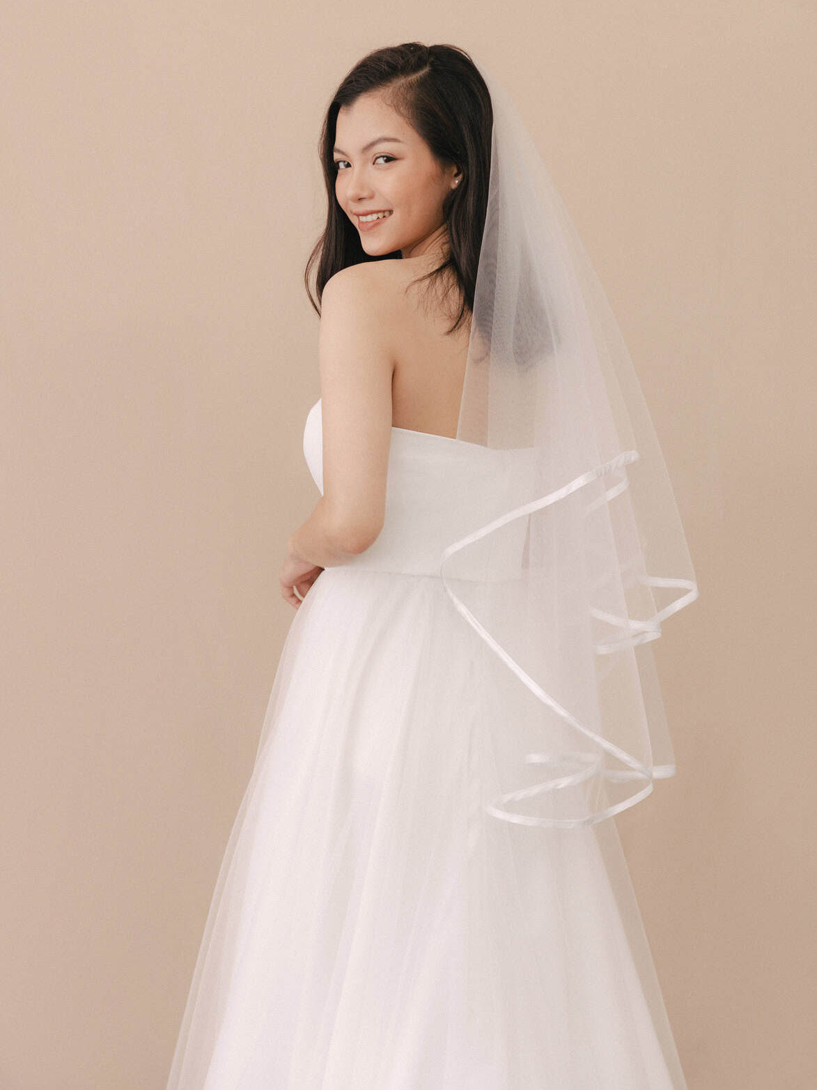 Woman wearing a white wedding dress with a veil against a beige background