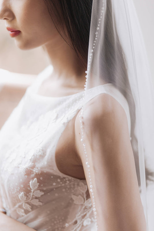 Close-up of a person wearing a white lace wedding dress with a veil.