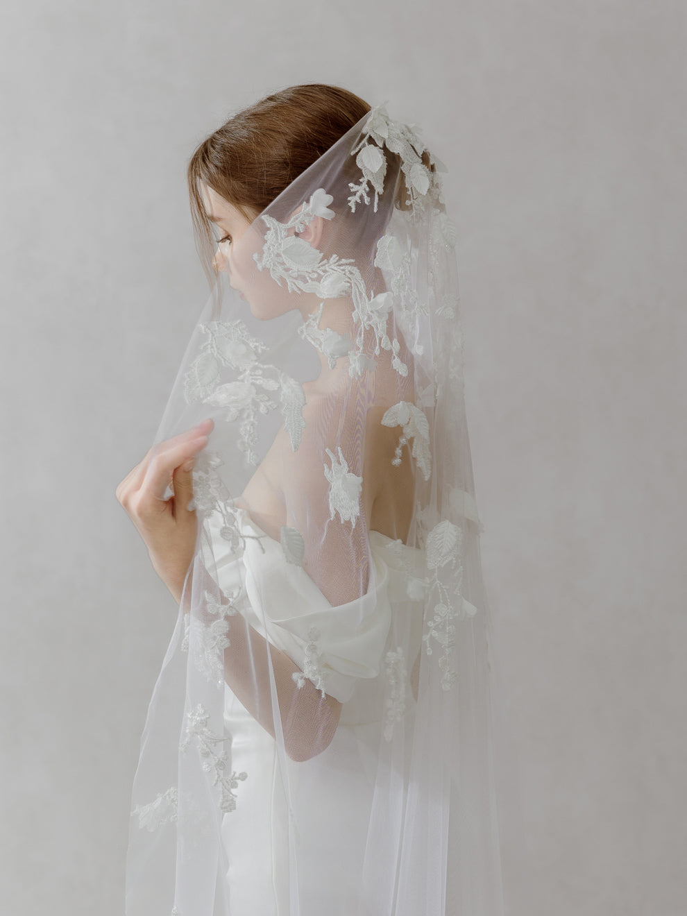 Woman wearing a white lace wedding veil against a plain background