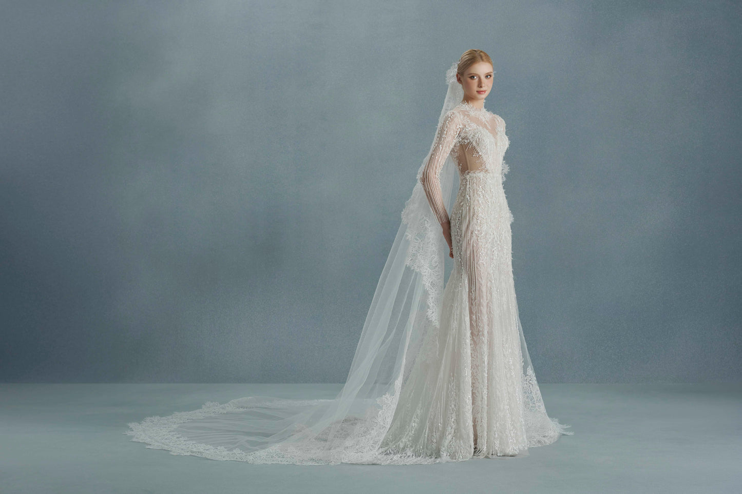 Woman wearing a white lace wedding dress with a long train against a gray background