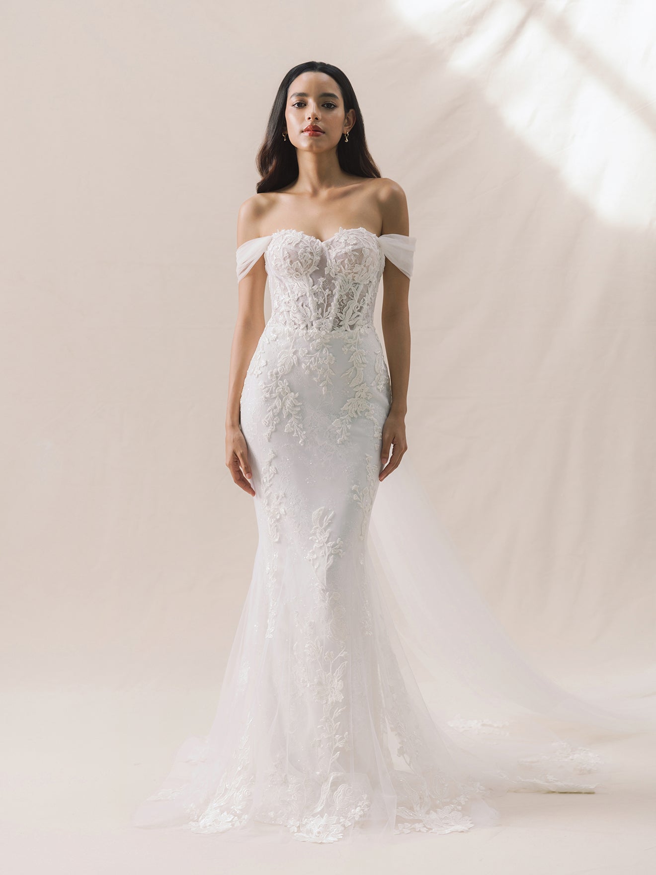 Woman wearing a white off-shoulder lace wedding dress against a neutral background