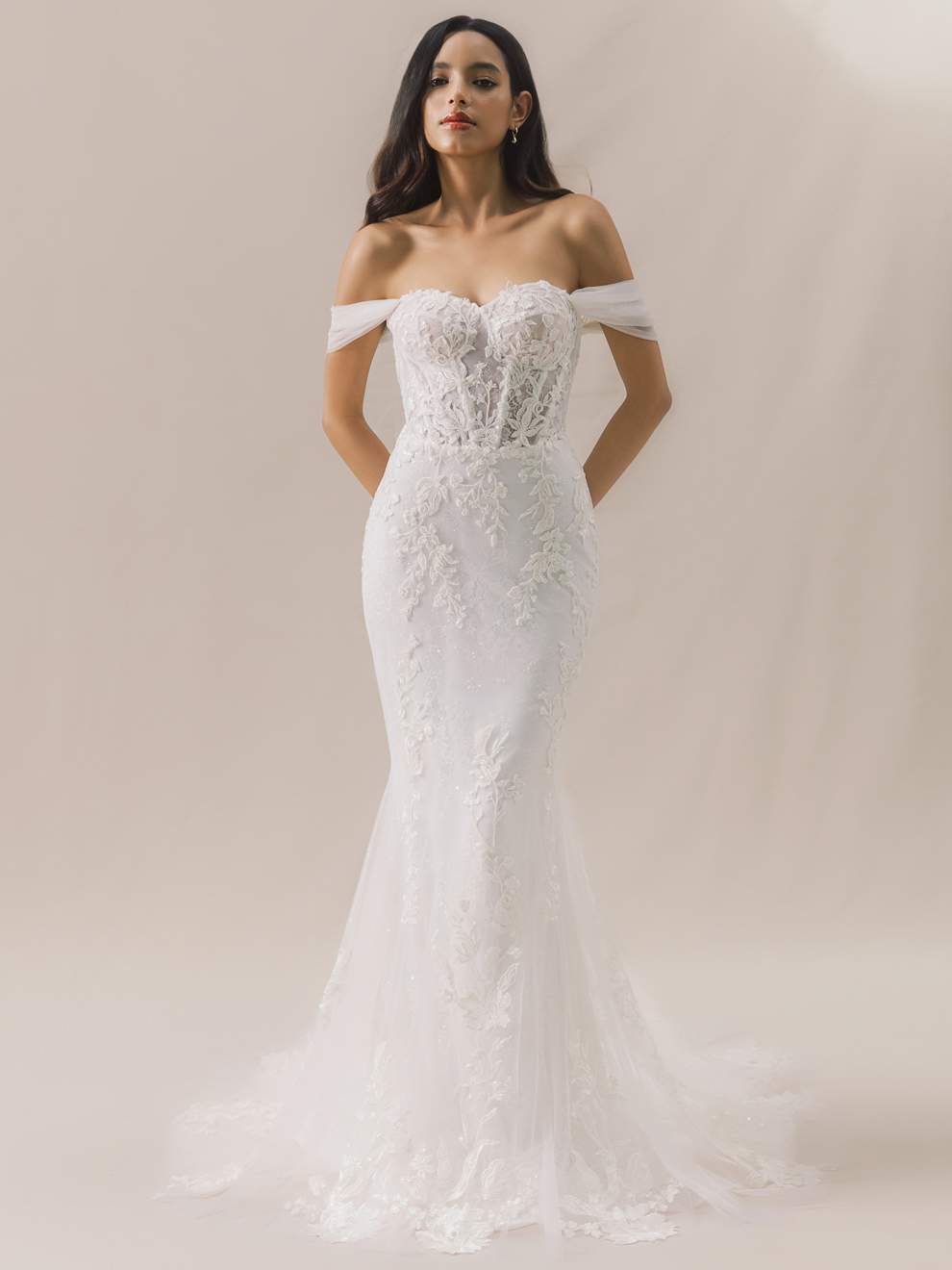 Woman wearing a white off-shoulder lace wedding dress against a plain background