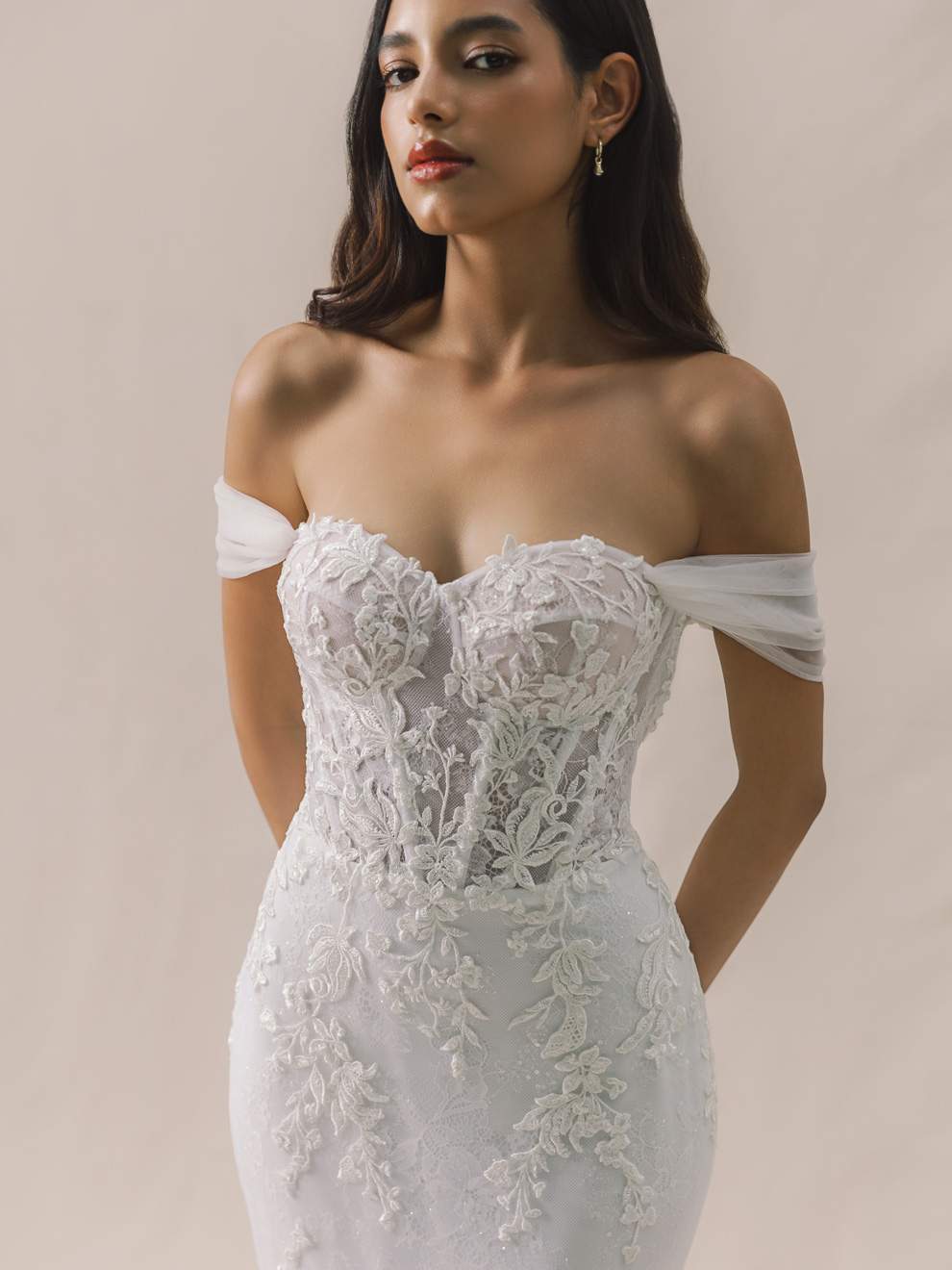 Woman wearing a white lace off-shoulder dress against a beige background