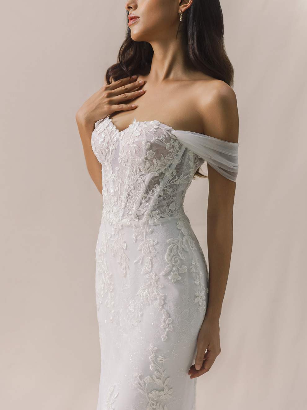Woman wearing a white lace wedding dress against a neutral background