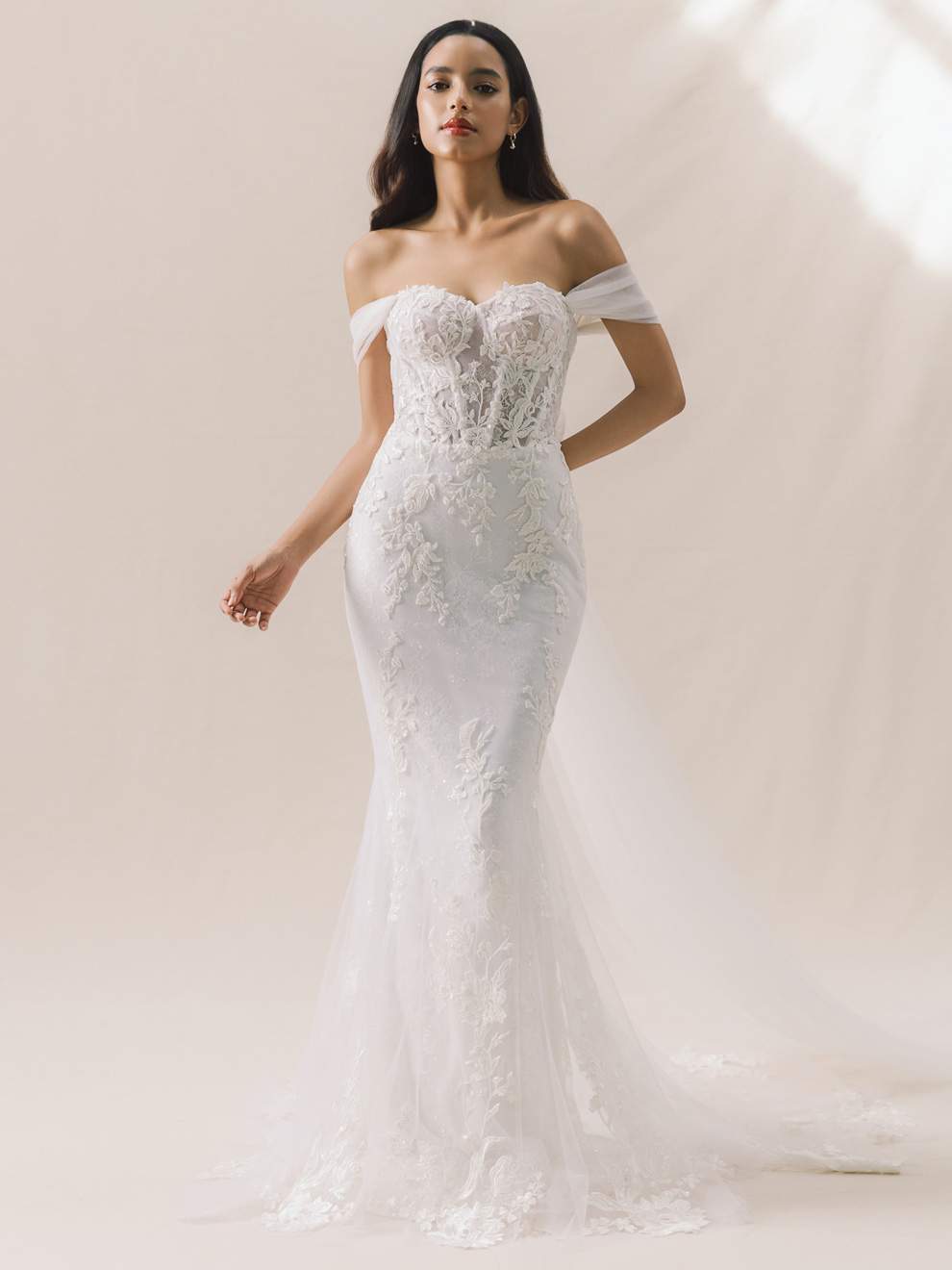 Woman wearing a white off-shoulder lace wedding dress against a plain background