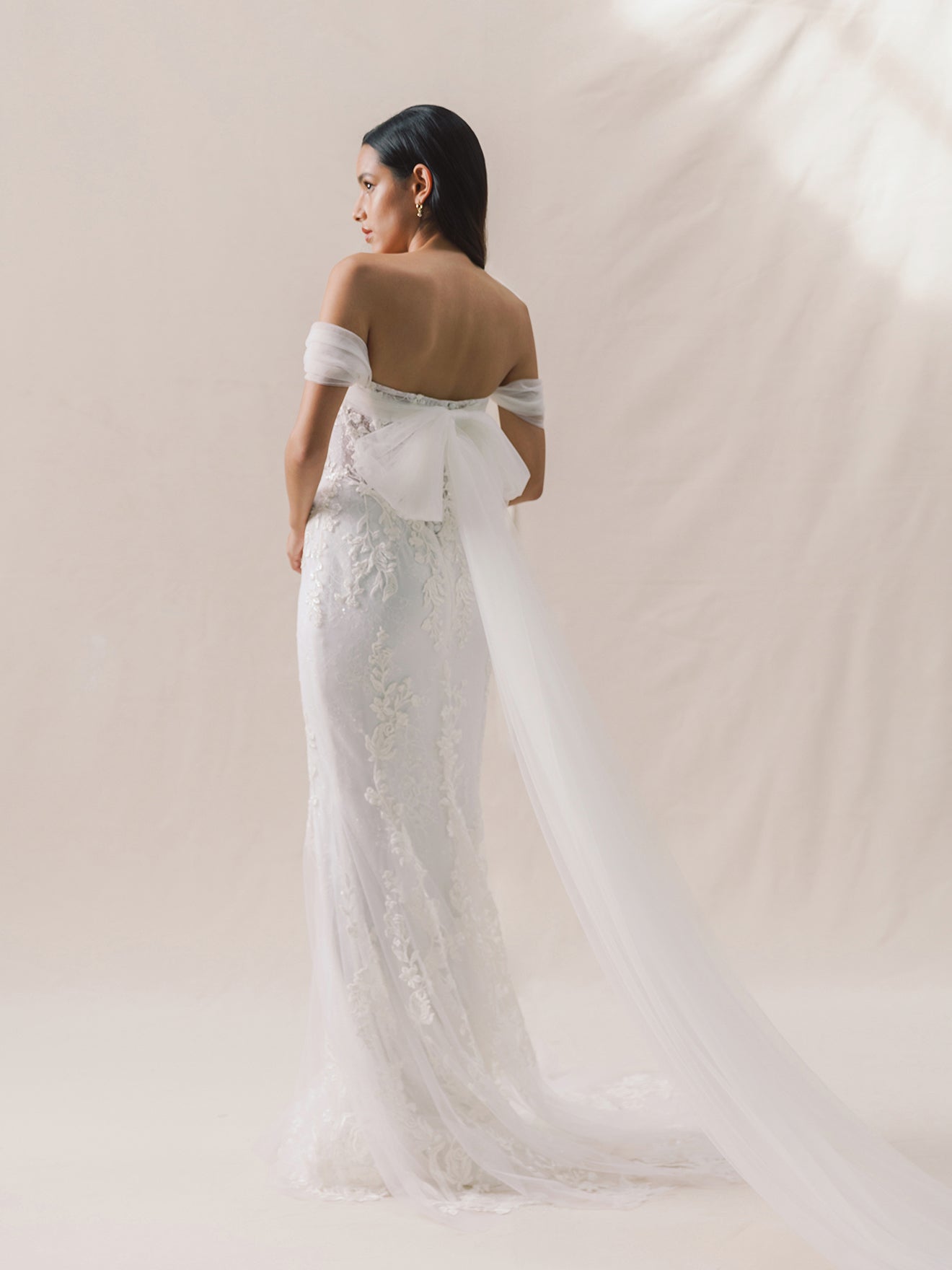 Woman wearing a white lace wedding dress against a plain background