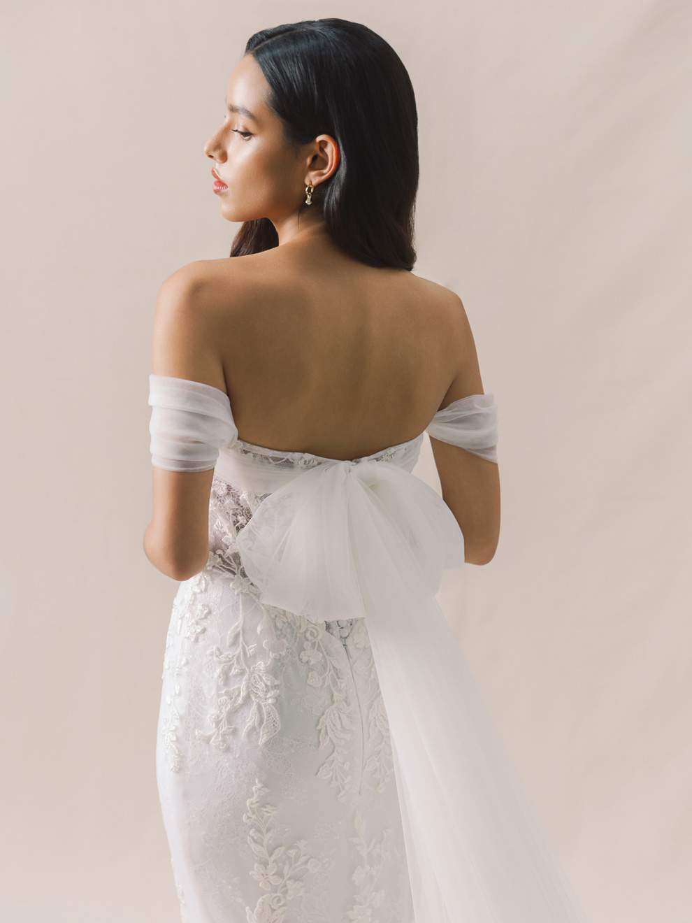 Woman wearing a white wedding dress with a bow detail on a plain background