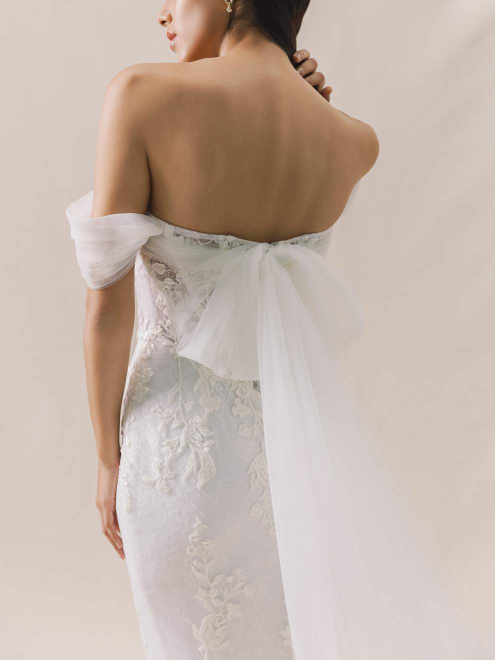 Woman wearing a strapless lace wedding dress with a sheer overlay against a plain background