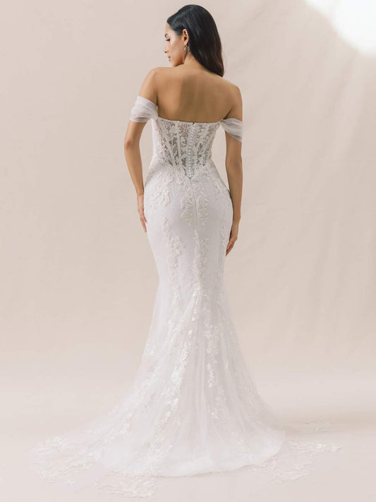 Woman wearing a white lace wedding dress against a plain background