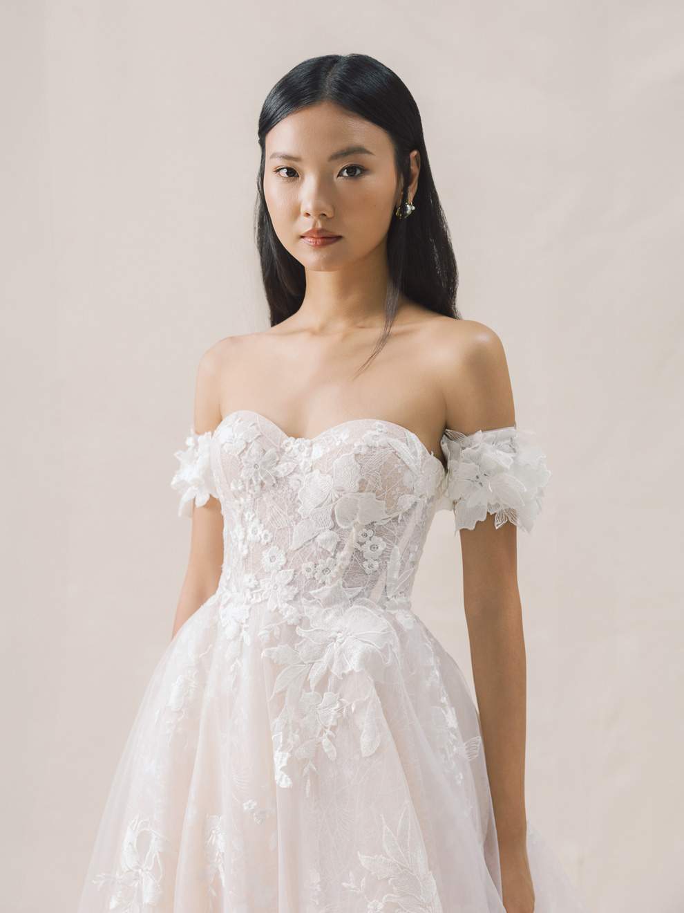 Woman wearing a white lace wedding dress against a plain background