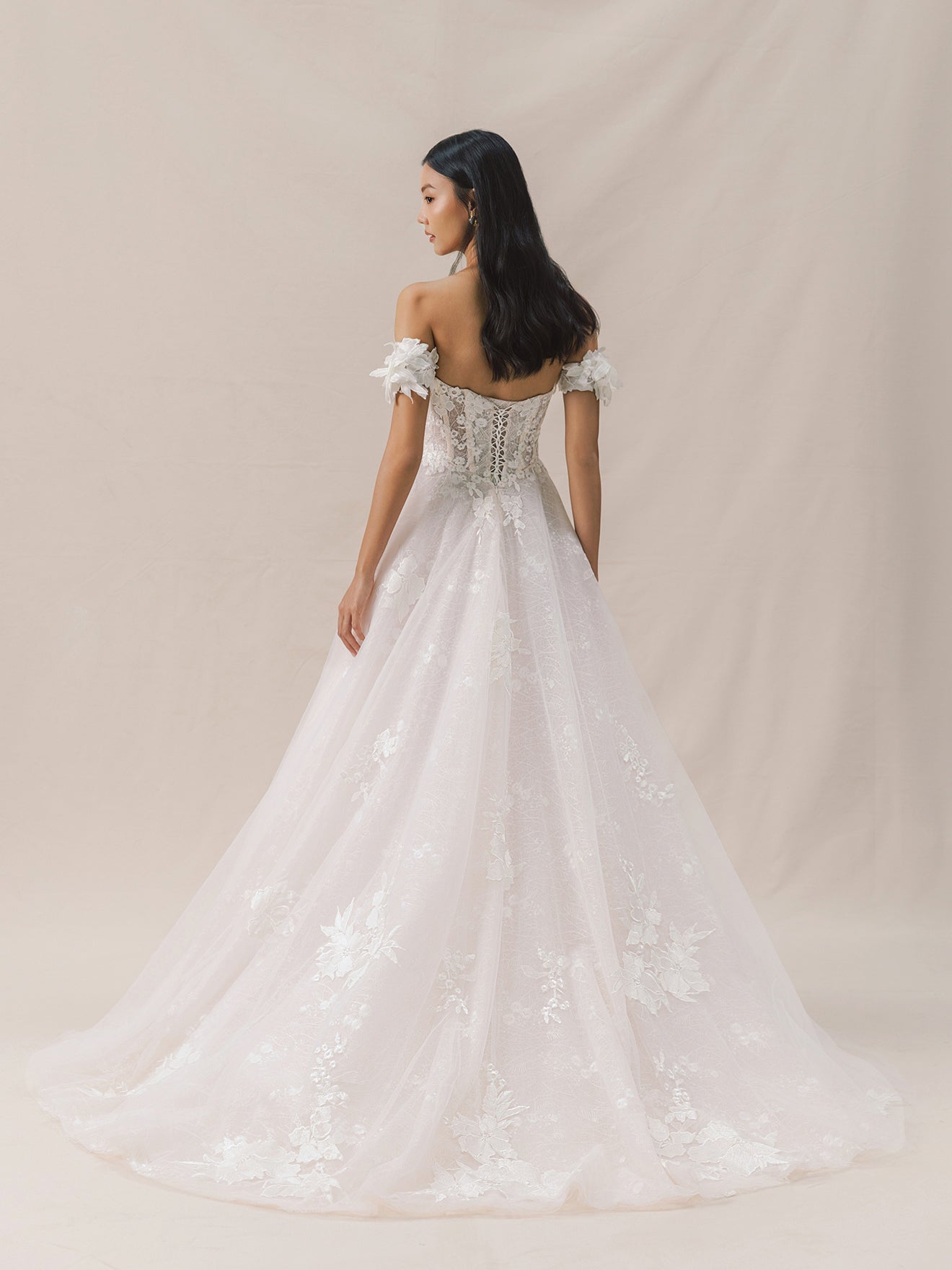 Woman wearing a white wedding dress with floral details against a beige background