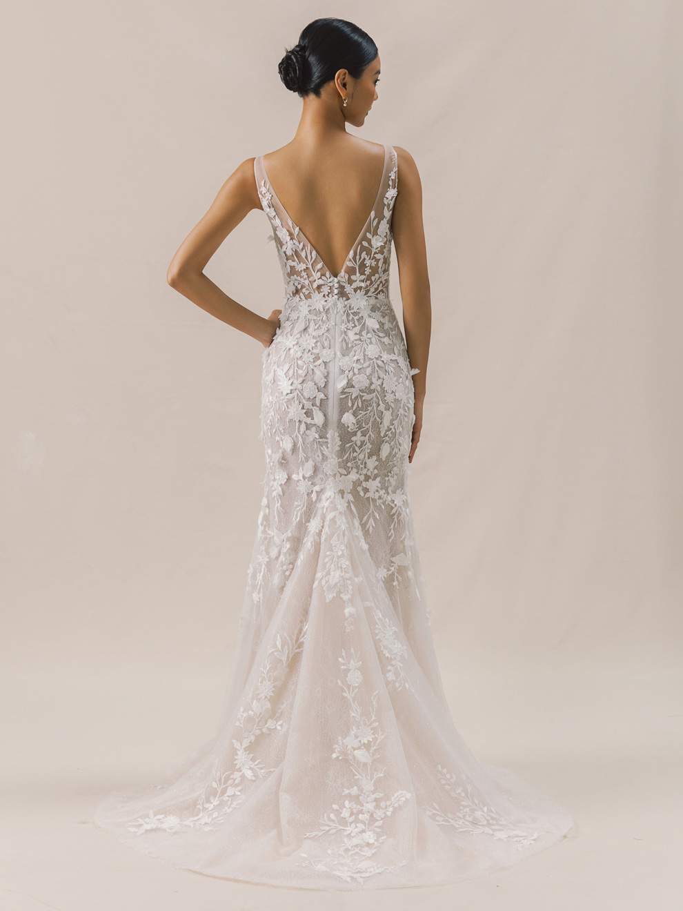 Woman wearing a white lace wedding dress with a low back on a beige background