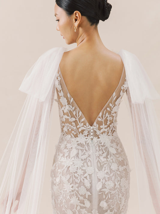 Back view of a lace wedding dress with a sheer overlay on a neutral background