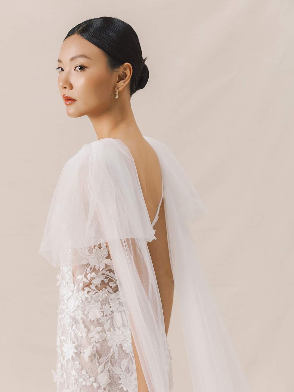 Woman wearing a white lace wedding dress with a sheer overlay against a beige background