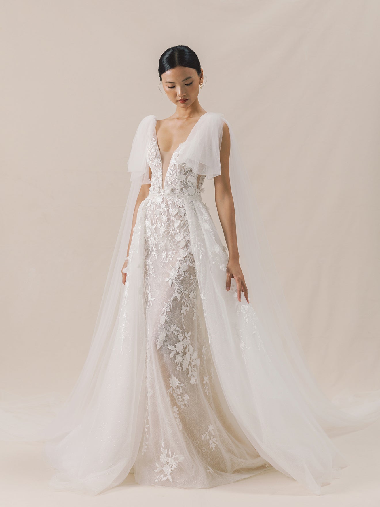 Woman wearing a white lace wedding dress against a plain background