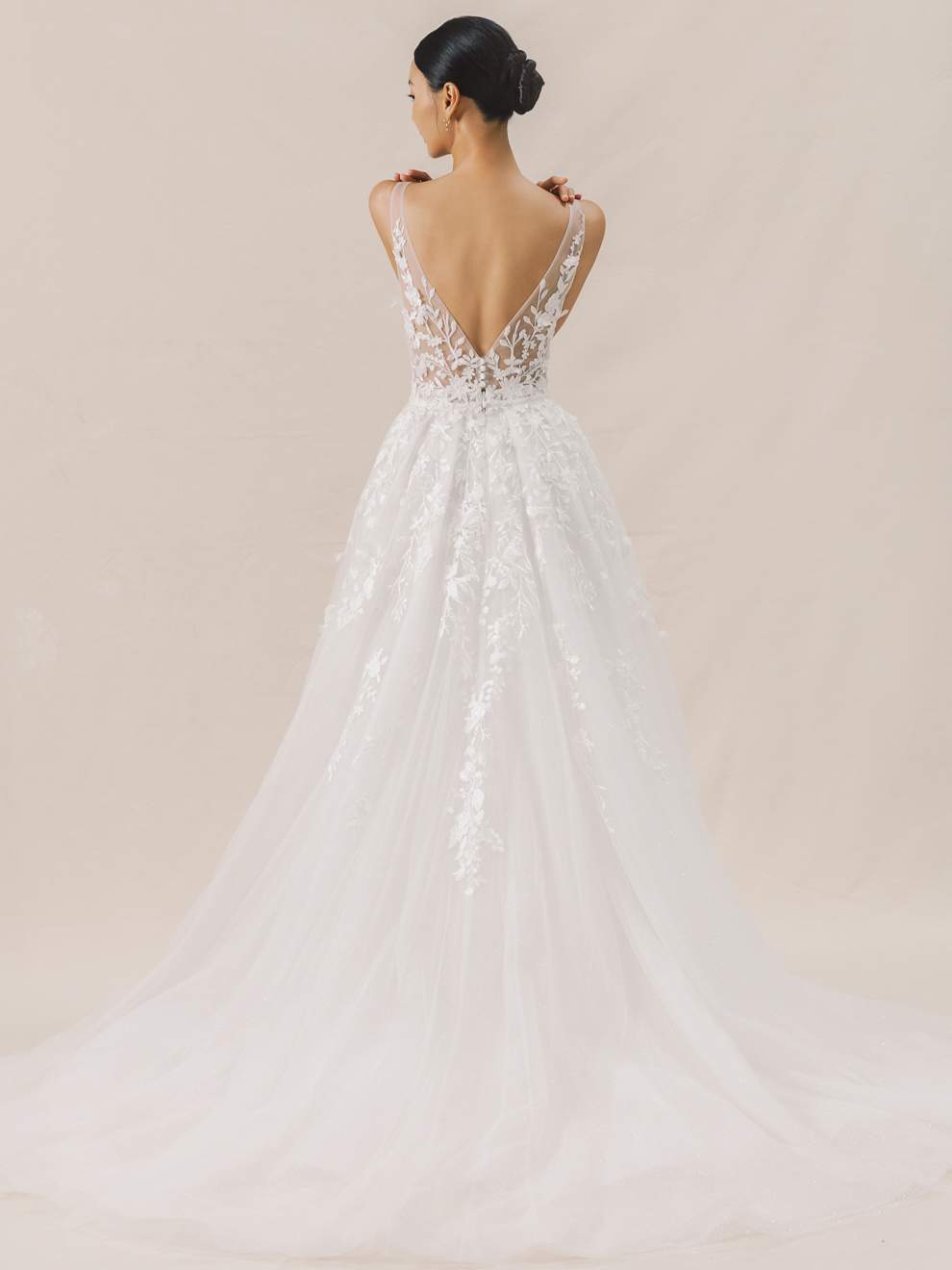 Woman wearing a white wedding dress with intricate detailing on a beige background