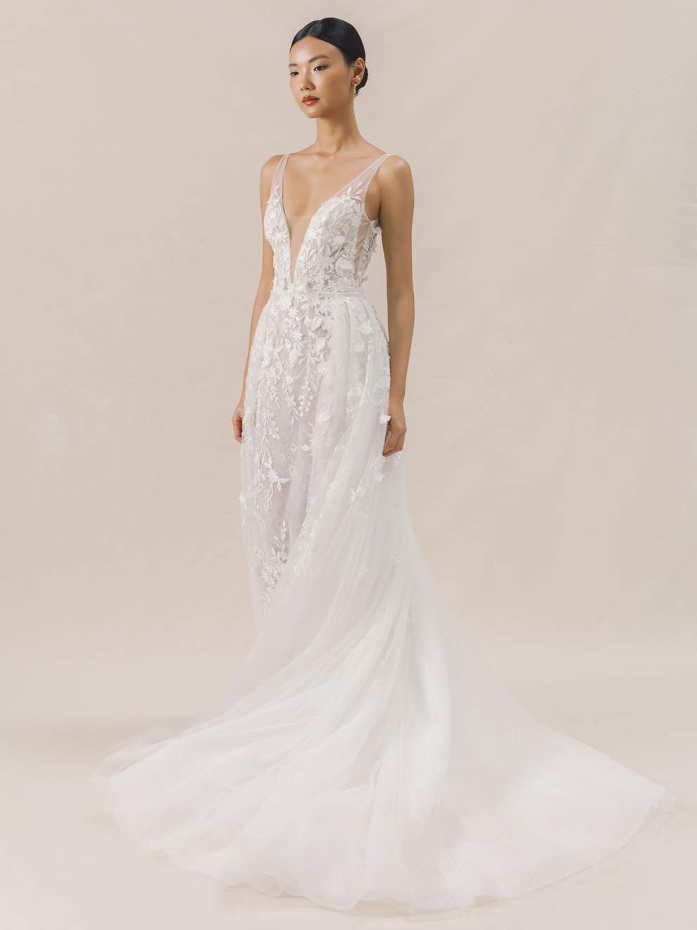 Woman wearing a white wedding dress with intricate detailing on a beige background