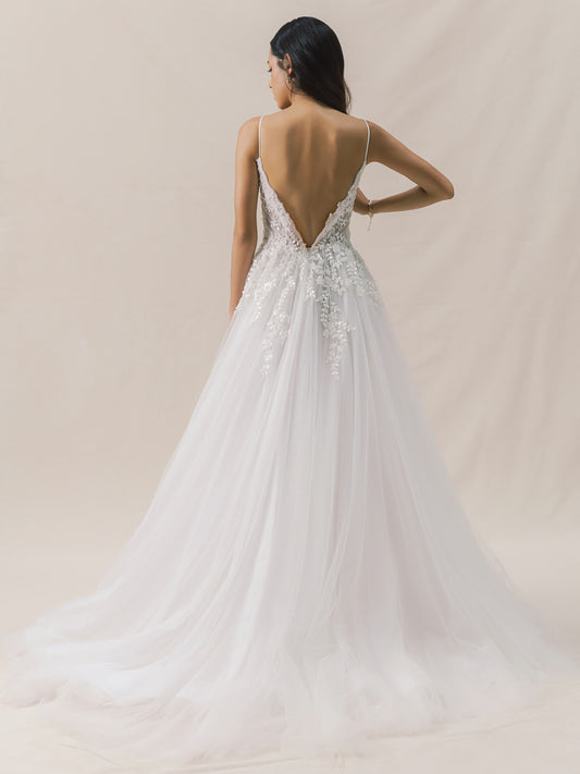 Woman wearing a white wedding dress with a low back and intricate detailing on a beige background