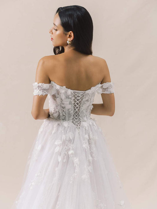 Woman wearing a white lace wedding dress with floral details on a beige background