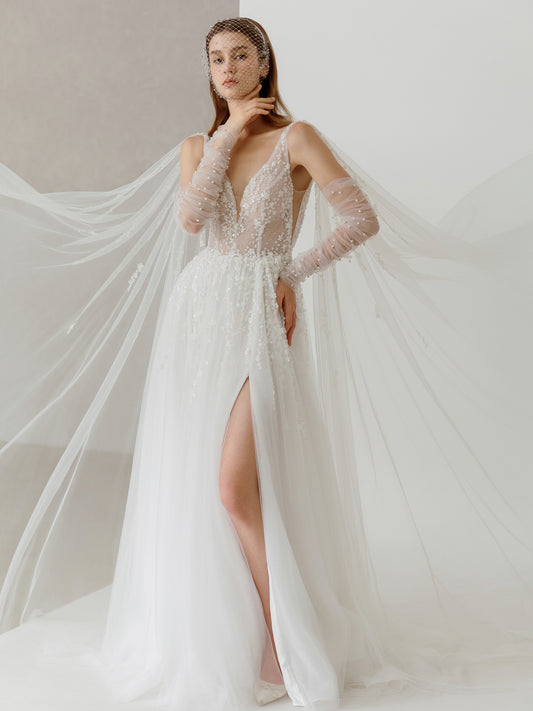 Woman wearing a white wedding dress with long sleeves and a slit skirt on a plain background