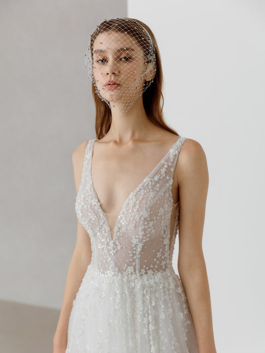 Woman wearing a white wedding dress with a sheer bodice and veil against a plain background