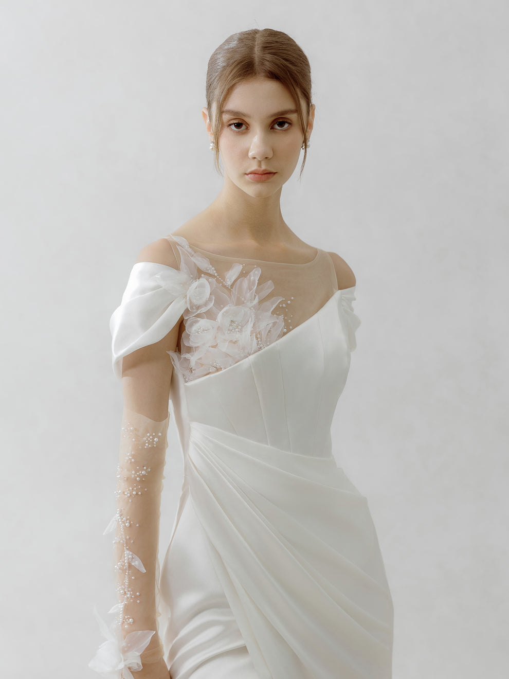Woman wearing a white wedding dress with floral details on a plain background