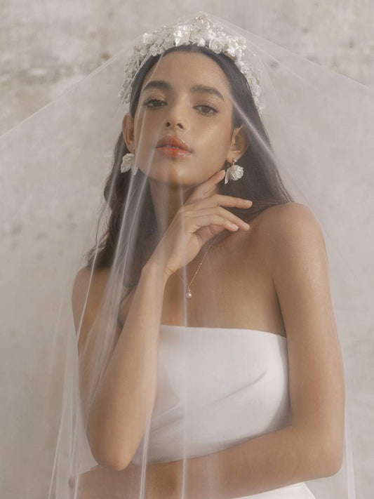 Woman wearing a white wedding dress with a veil and floral headpiece against a neutral background