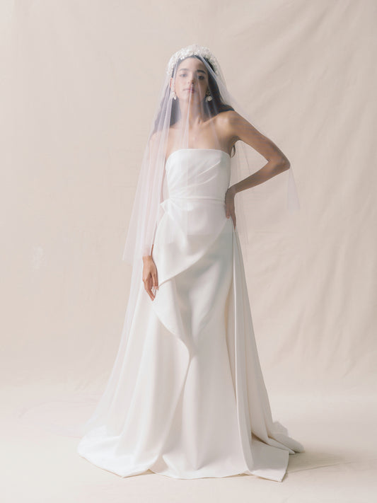 Woman wearing a white wedding dress with a long train and veil on a plain background