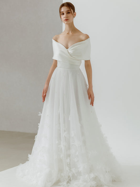 Woman wearing a white off-shoulder wedding dress against a plain background