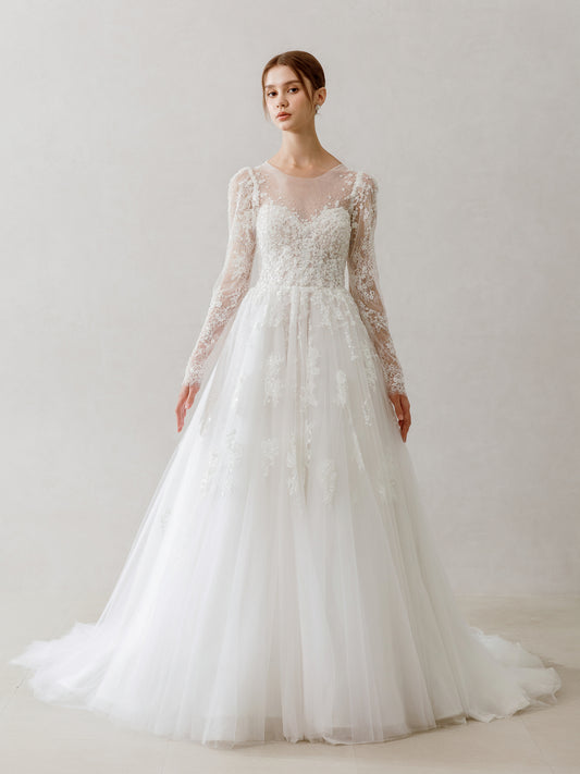 Model wearing a white lace wedding dress with long sleeves against a plain background