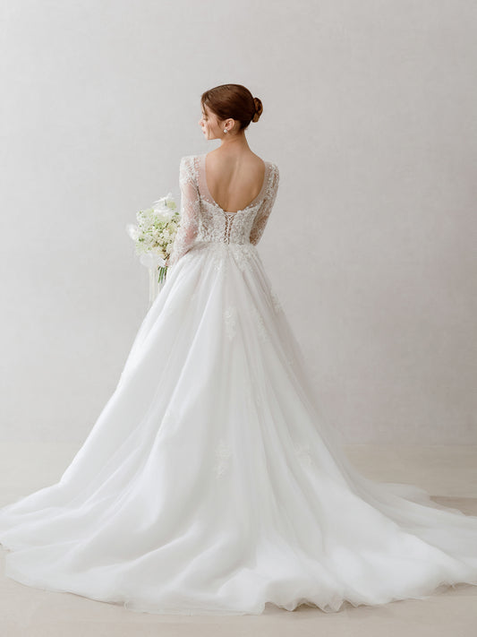 Woman wearing a white wedding dress with lace details on a plain background