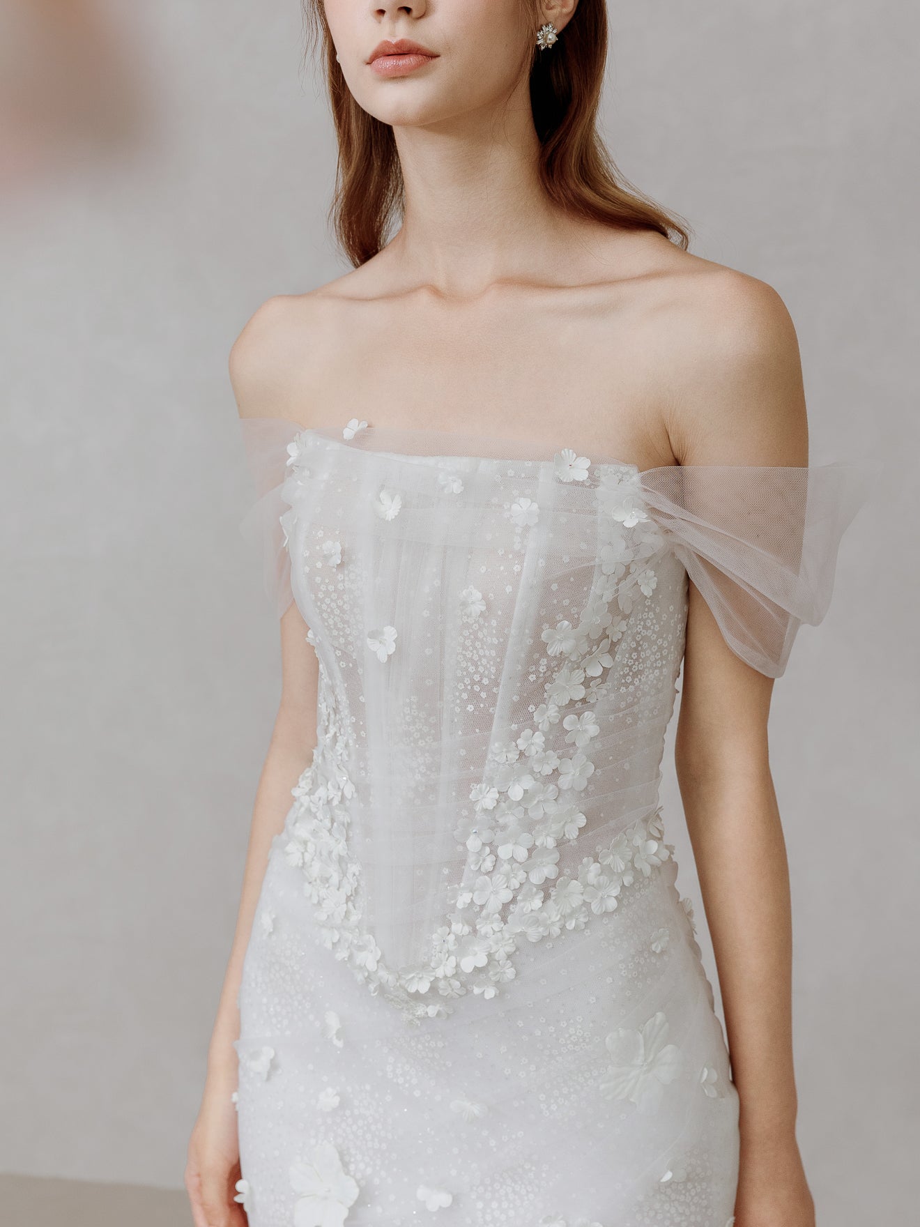 Woman wearing a white wedding dress with floral details on a plain background