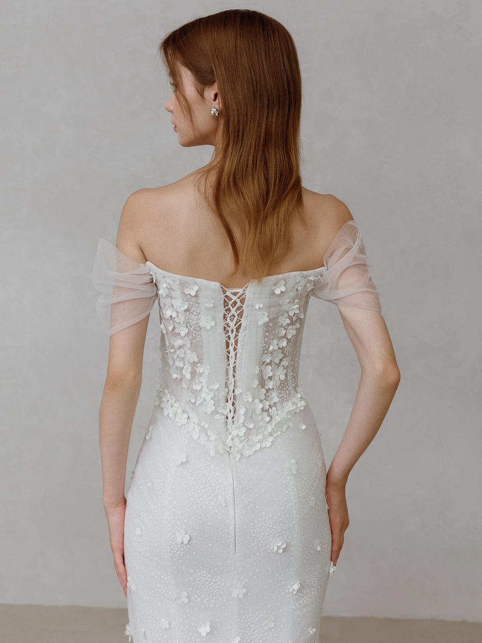 Woman wearing a white lace wedding dress with sheer sleeves against a plain background