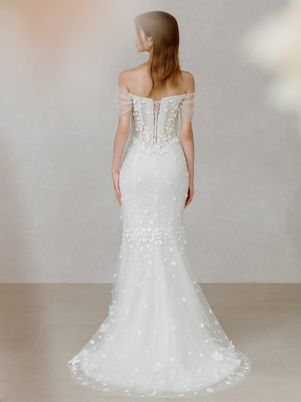 Woman wearing a white off-shoulder wedding dress with floral details on a plain background