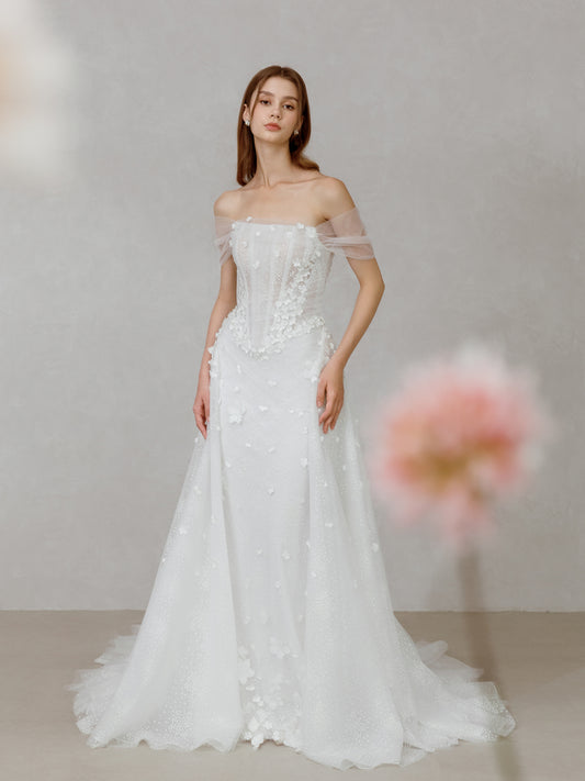 Woman wearing a white wedding dress with floral details against a neutral background