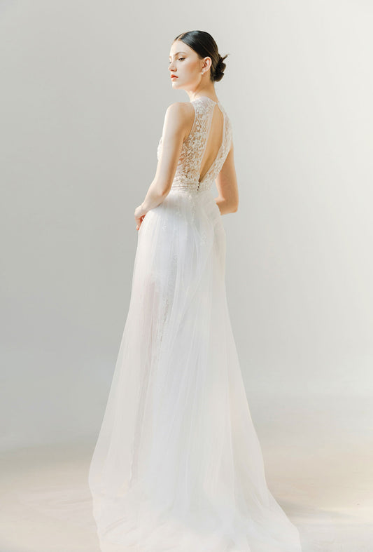 Woman wearing a white wedding dress with a sheer back on a plain background