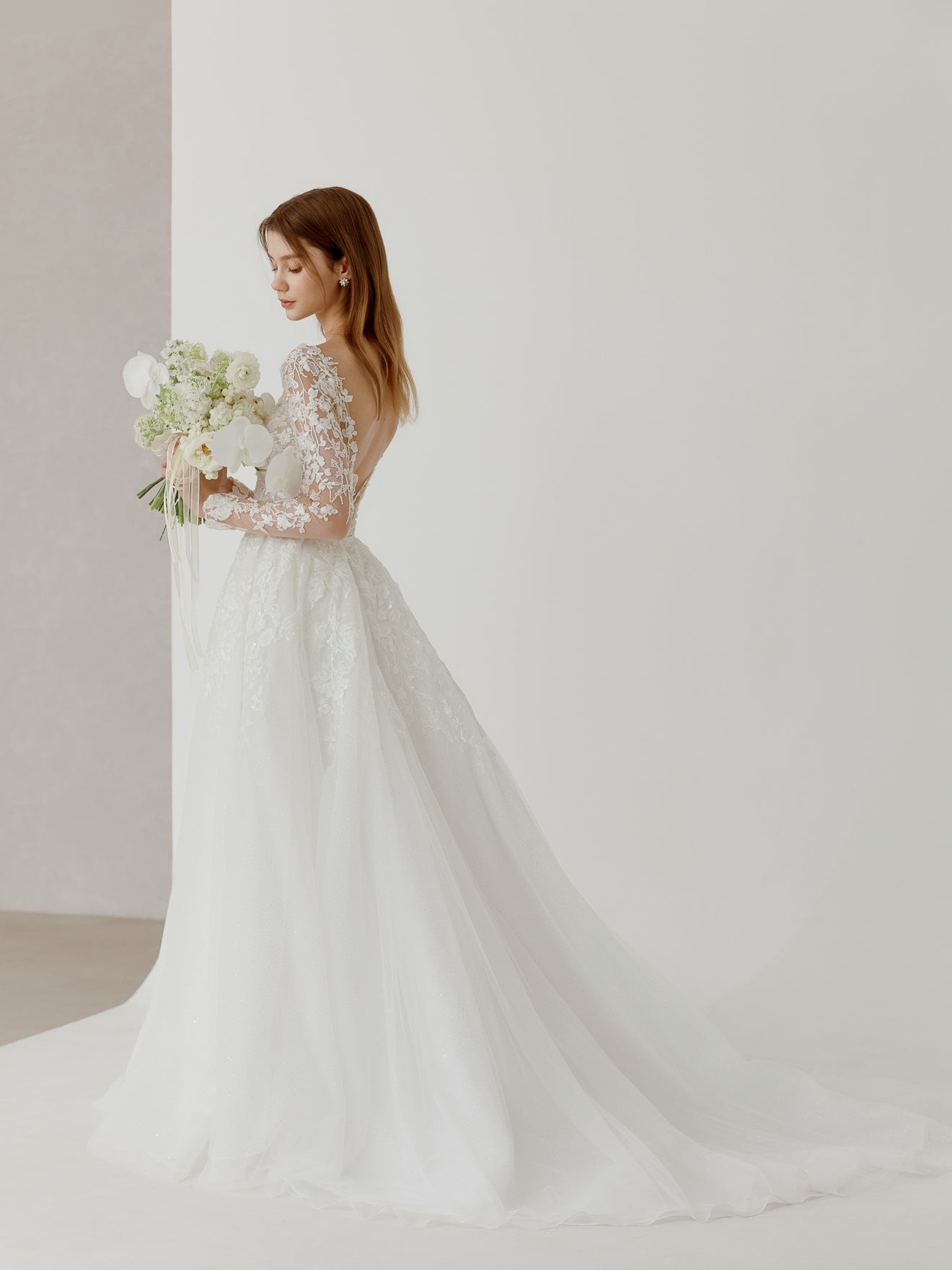 Woman in a white wedding dress holding a bouquet against a plain background