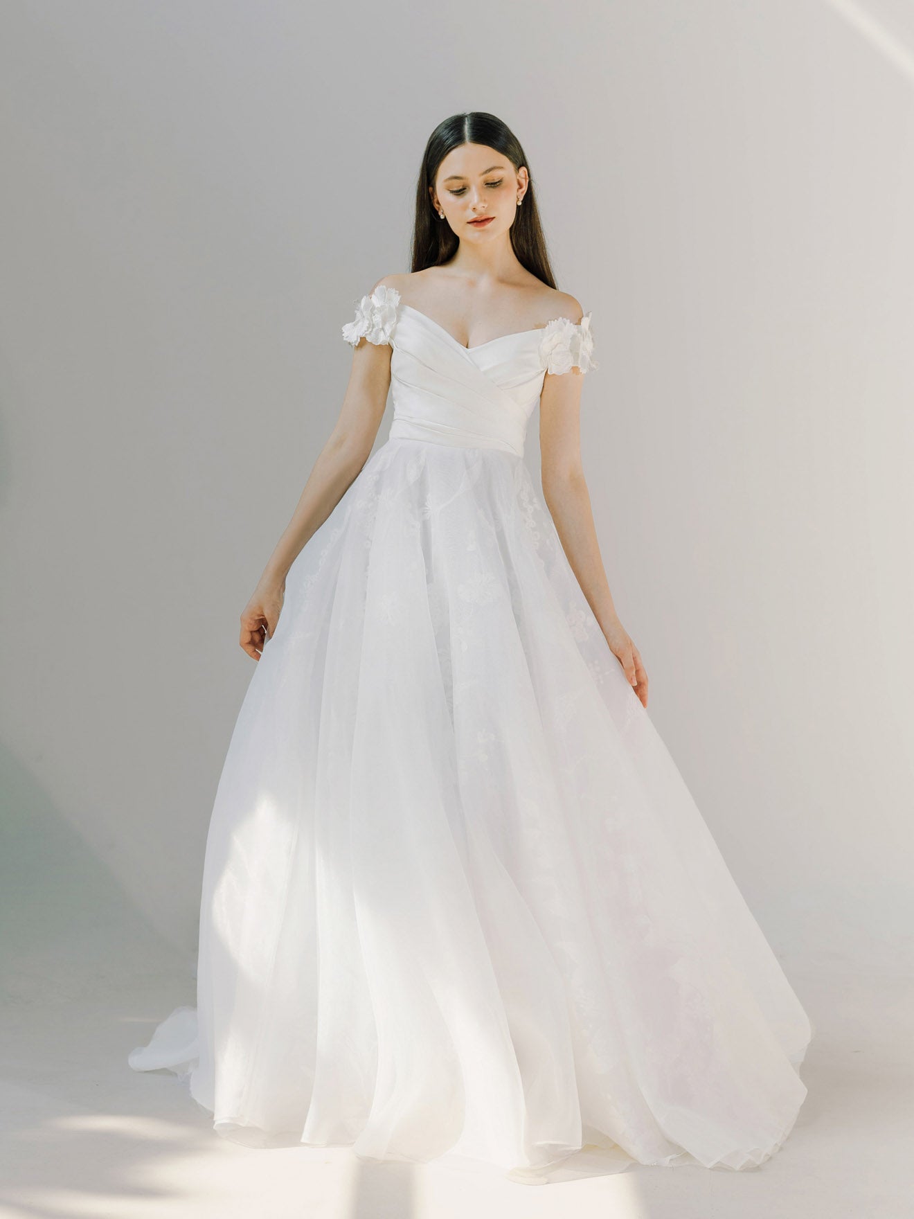 Woman wearing a white wedding dress with floral details on a plain background