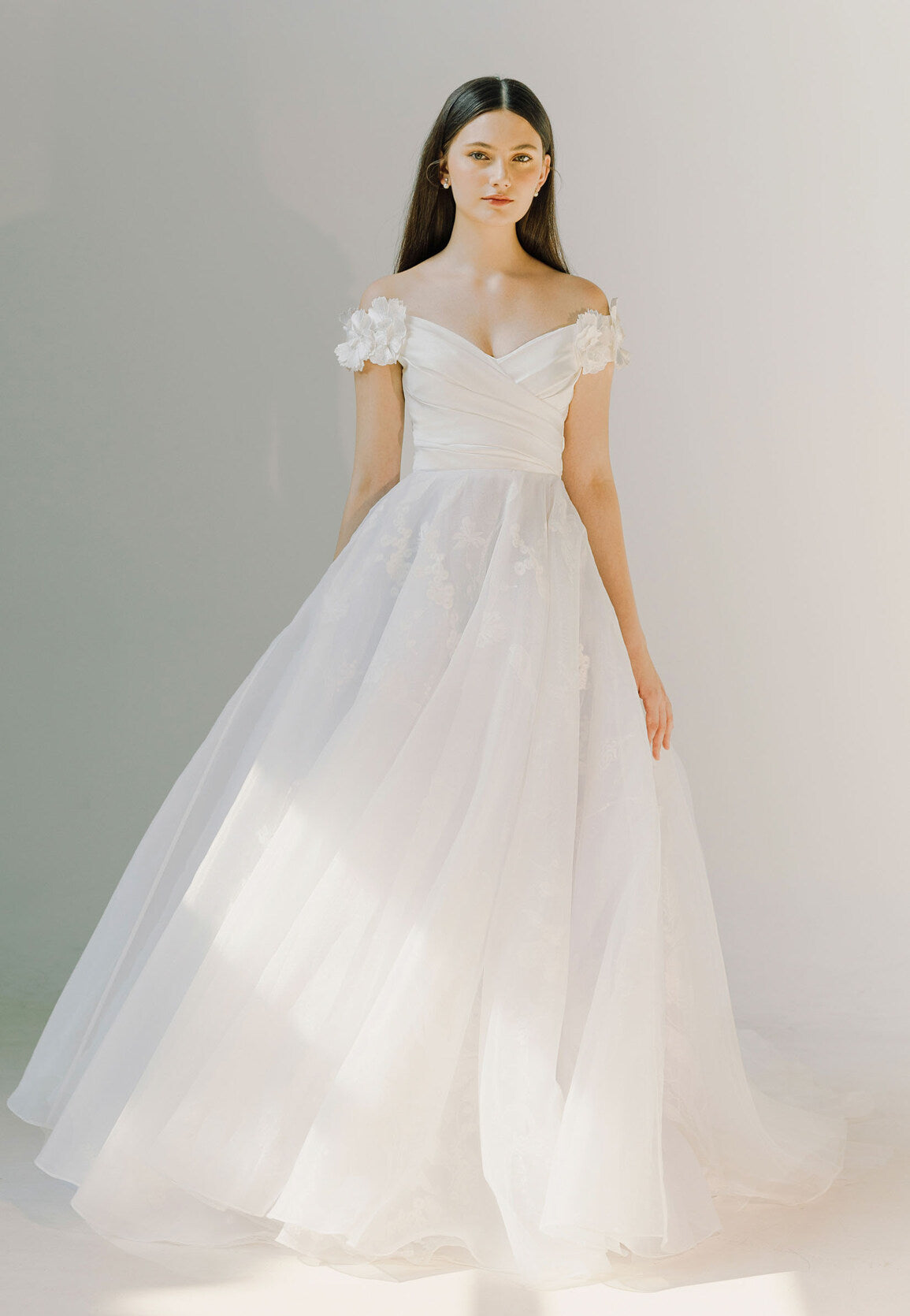 Woman wearing a white wedding dress with floral details on a plain background
