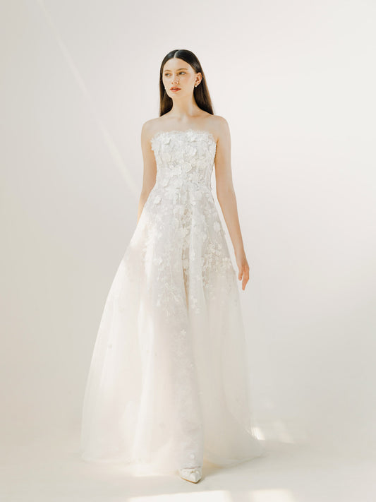 Woman wearing a white strapless dress with floral details against a plain background